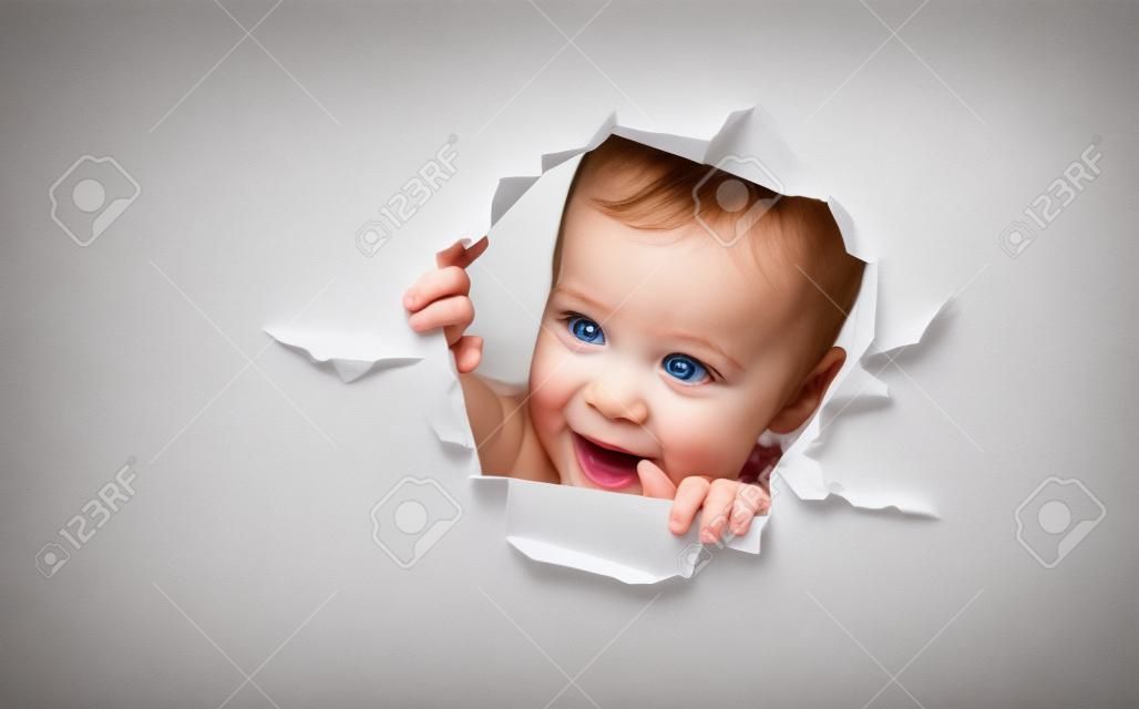 Drôle bébé enfant fille lorgnant à travers un trou dans un blanc affiche papier vide