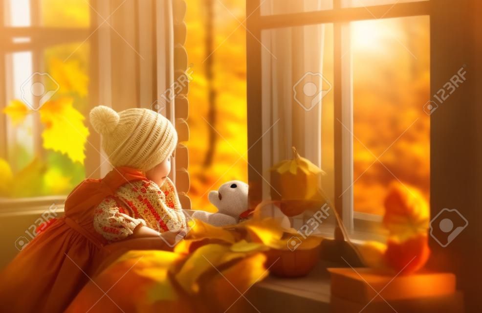 ребенок девочка, глядя через открытое окно в красивой природе осени золота