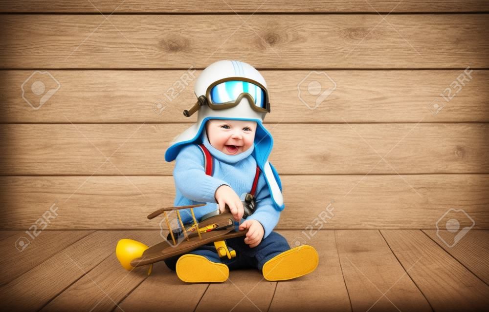 Neonato divertente pilota aviatore con l'aeroplano ridere su sfondo di legno