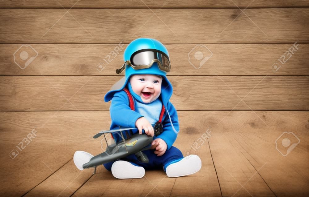 Neonato divertente pilota aviatore con l'aeroplano ridere su sfondo di legno