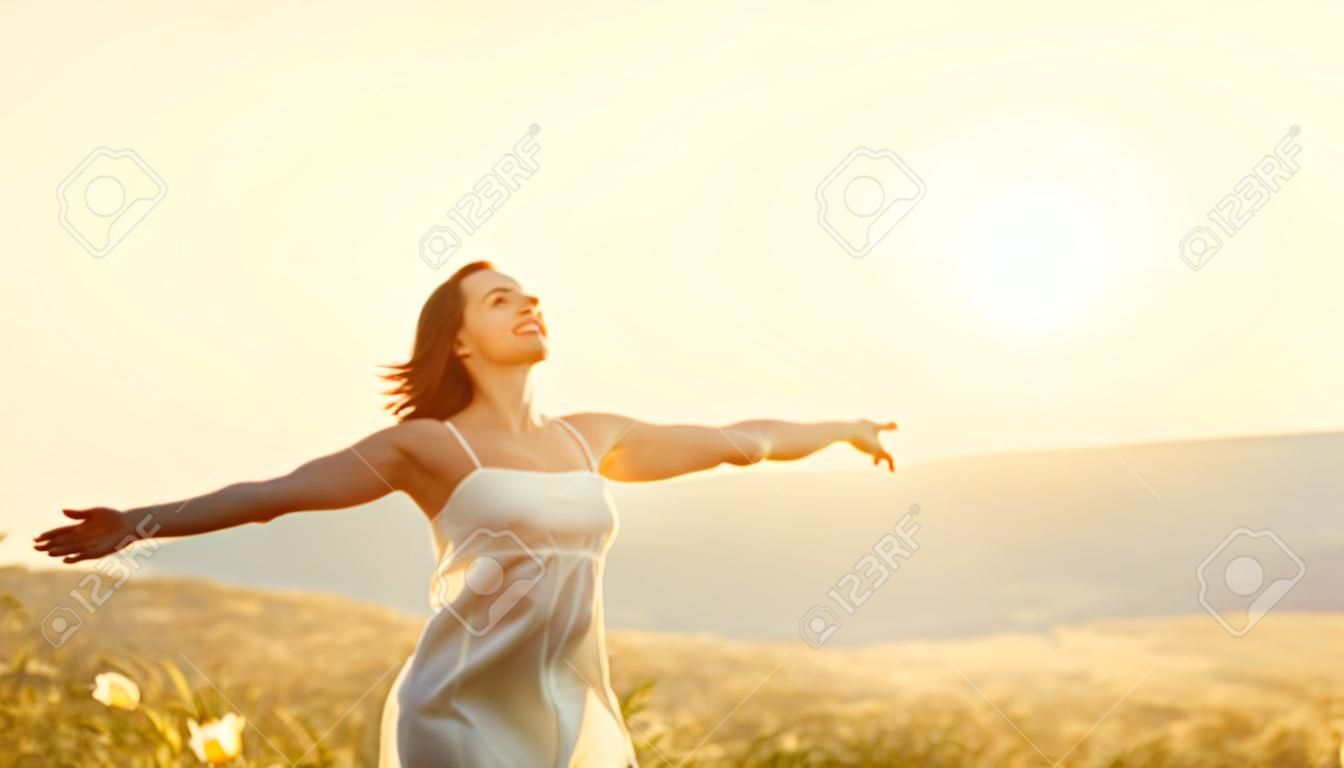 Mulher feliz, de costas para o pôr do sol na natureza no verão, com as mãos abertas