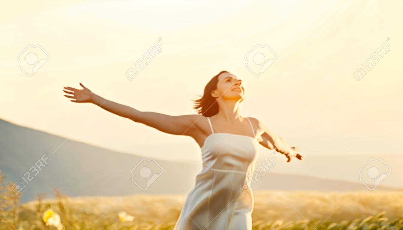 Szczęśliwa kobieta, stojąca z plecami na zachodzie słońca w przyrodzie w lecie z otwartymi dłońmi