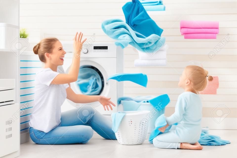 Happy family mother housewife and child daughter in laundry with washing machine 
