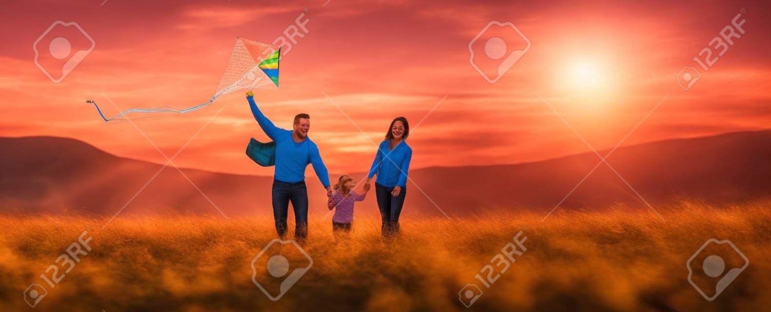 La figlia felice del padre, della madre e del bambino della famiglia lancia un aquilone sulla natura al tramonto