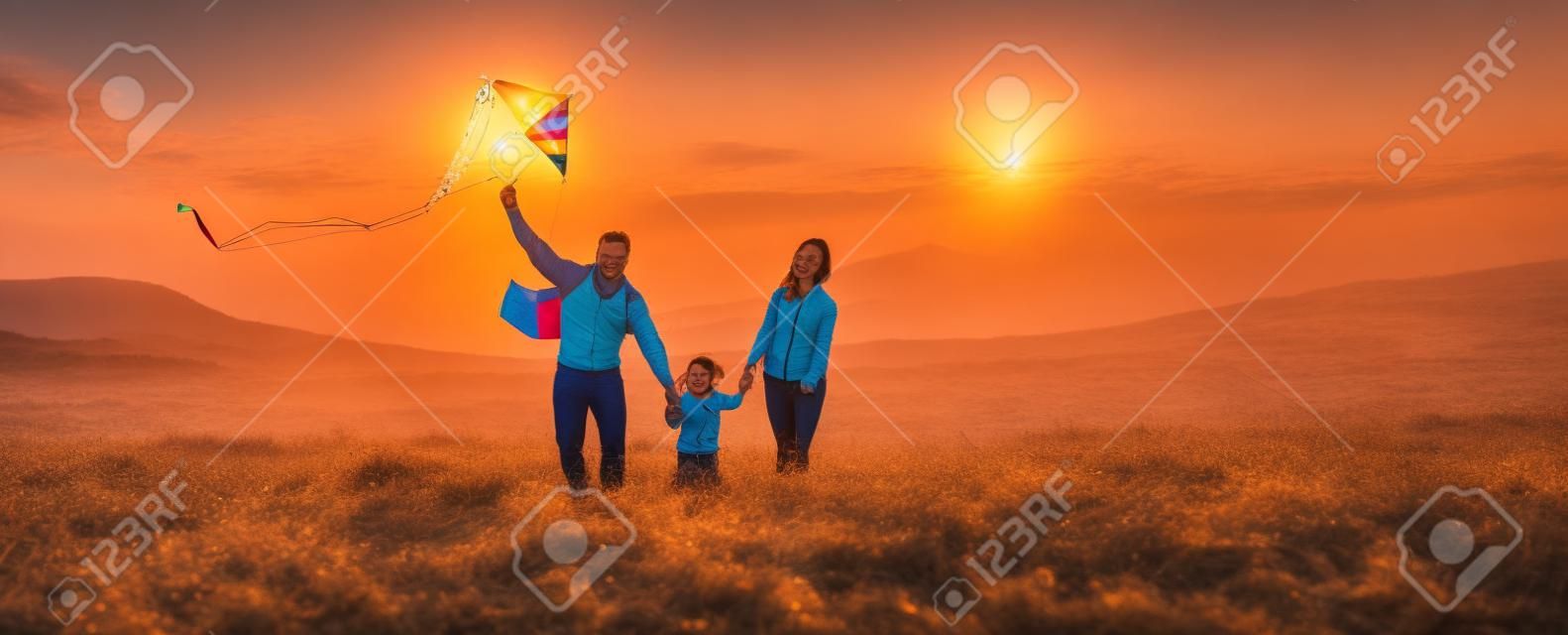 Gelukkige familie vader, moeder en kind dochter lanceren een vlieger op de natuur bij zonsondergang