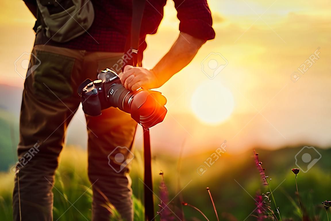 旅行写真家。自然界の夕暮れ時に山の中でカメラを持つ男の旅行者