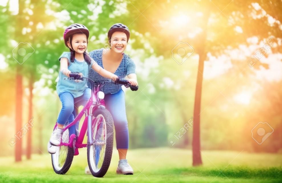 szczęśliwa mama rodziny uczy córkę jeździć na rowerze w parku w przyrodzie