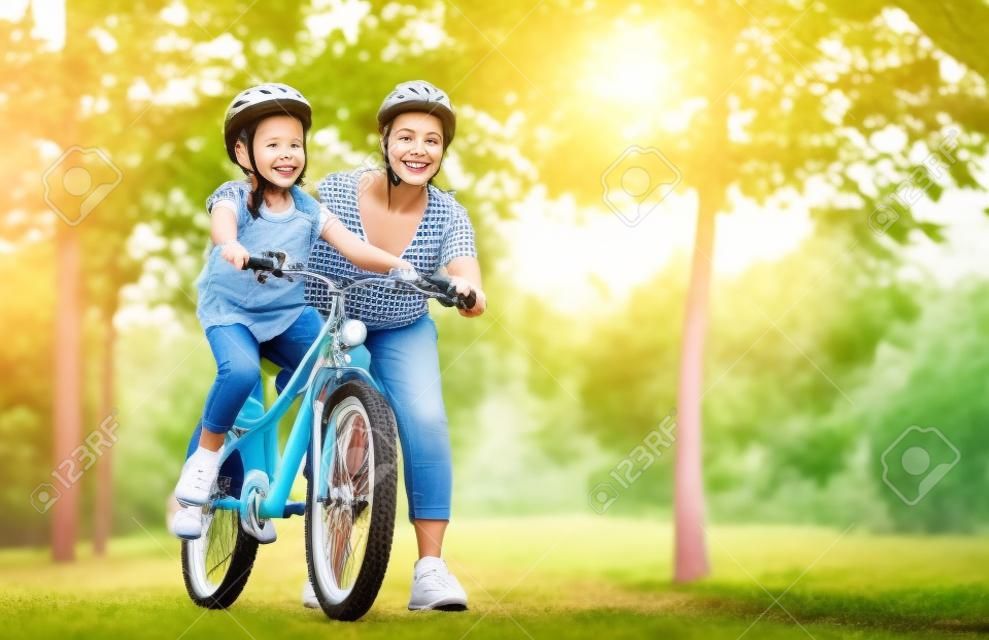 szczęśliwa mama rodziny uczy córkę jeździć na rowerze w parku w przyrodzie
