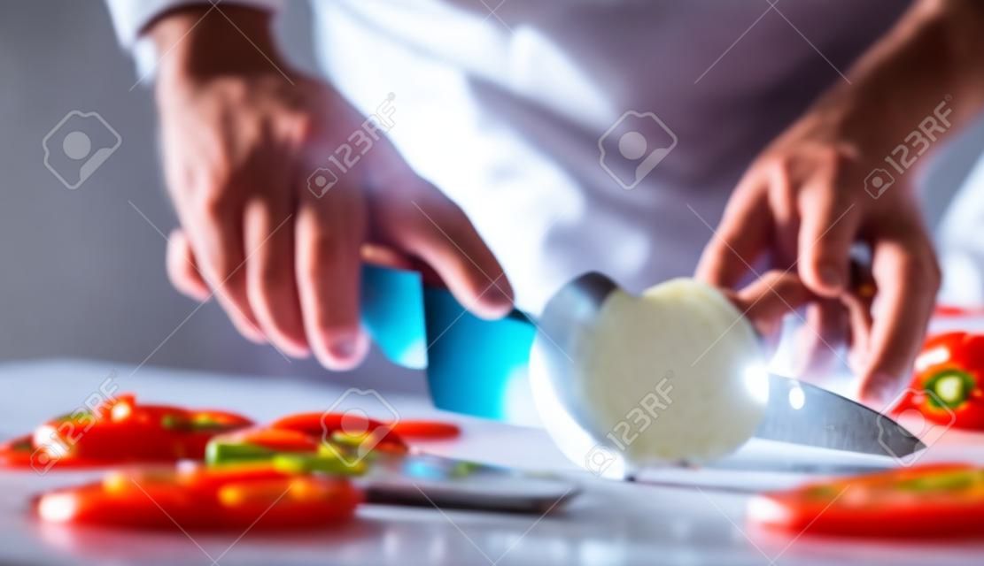 Koch schneidet Gemüse und Tomaten auf dem Tisch im Restaurant. Prozess des Schneidens und Zubereitens von Speisen in der Küche.