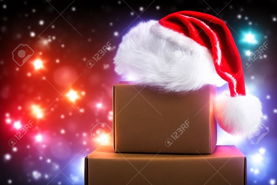 Scatola di trasporto marrone vuota con cappello di Babbo Natale in cima con luci di Natale sullo sfondo.