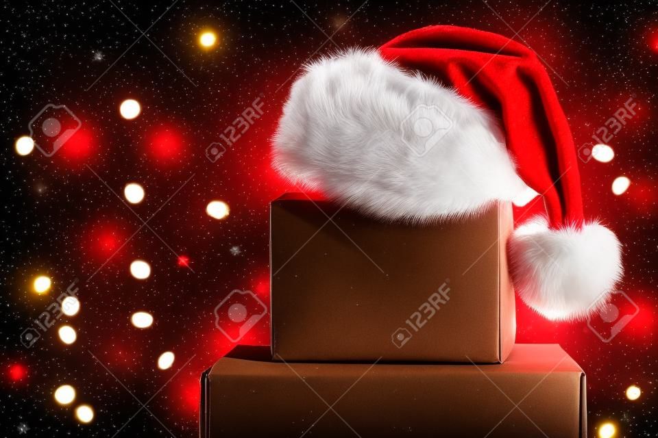 Boîte de fret marron vierge avec chapeau de Père Noël sur le dessus avec des lumières de Noël sur fond.