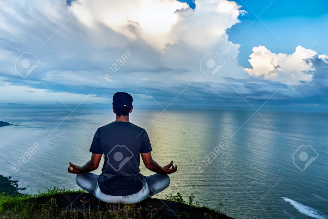 man meditating at hilltop with amazing landscape and sea horizon at morning image is taken at gokarna karnataka india. the view from here is pristine and mesmerizing.