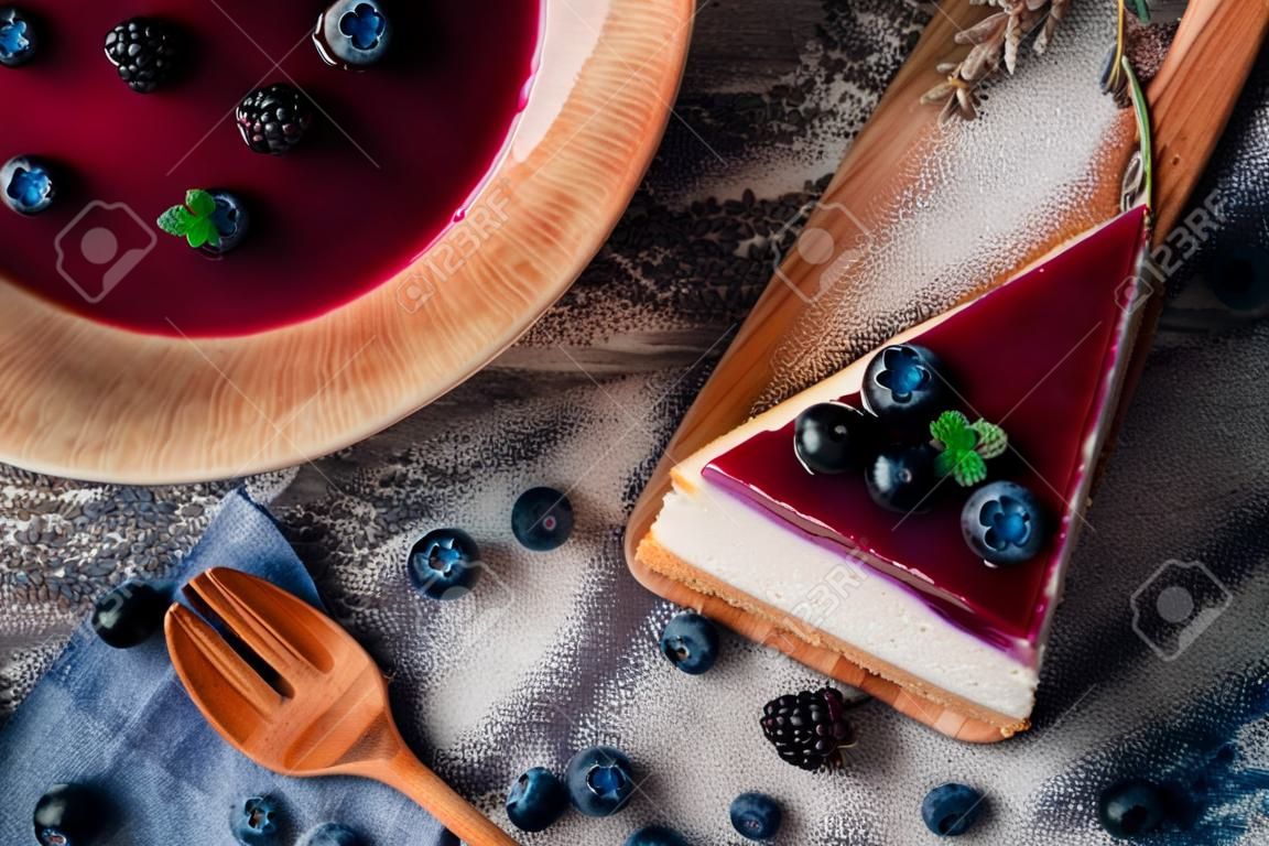 Cheesecake de mirtilo cremoso doce com bagas azuis frescas em um fundo de madeira azul.