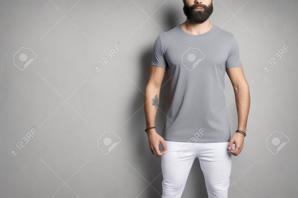 Modello di uomo muscoloso barbuto che indossa una t-shirt bianca vuota con spazio per il tuo logo o design in stile urbano casual su sfondo bianco. Colpo dello studio.