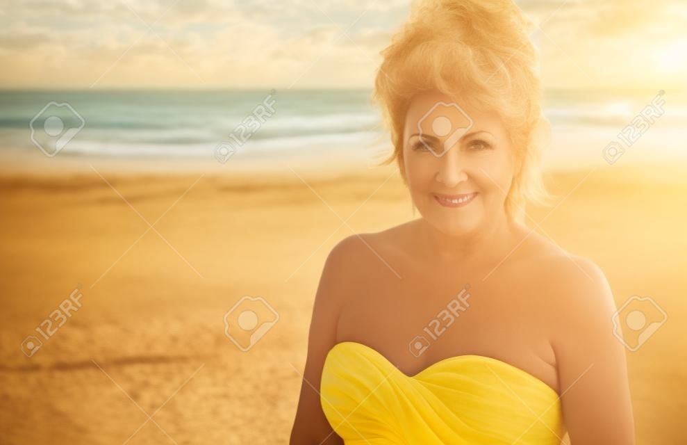 Outdoor Portrait of a Beautiful Mature Woman on the beach wearing a yellow top.