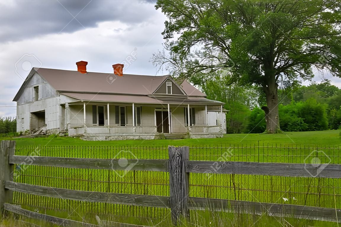 Abandoned Rural Farmhouse with Wooden Fence and Large Tree in Yard