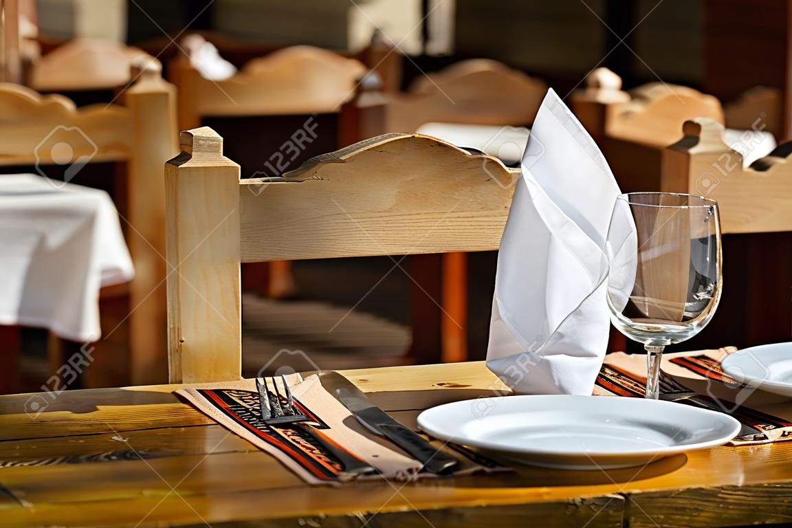 Two empty white plates, two glasses with napkins standing on a wooden table. Street restaurant.