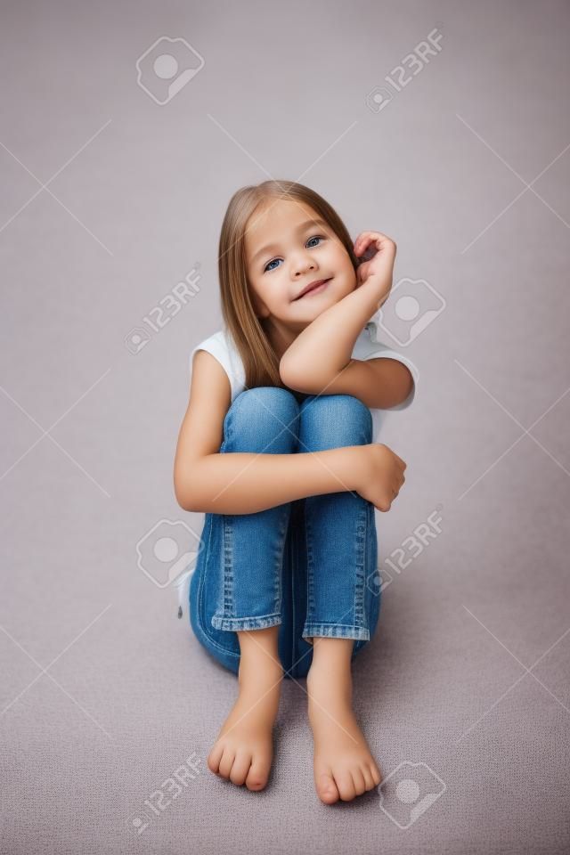 close-up beeld van een mooi klein meisje zitten op de vloer in jeans