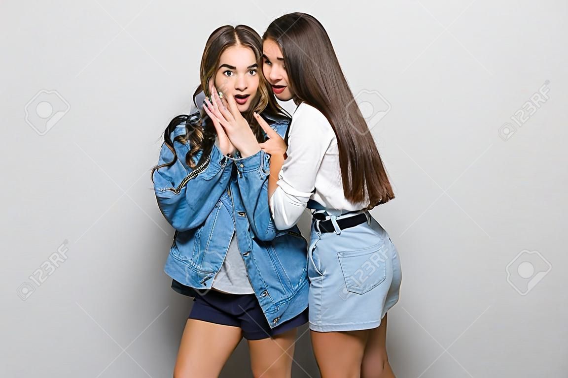 Portrait of two girls gossip on gray background