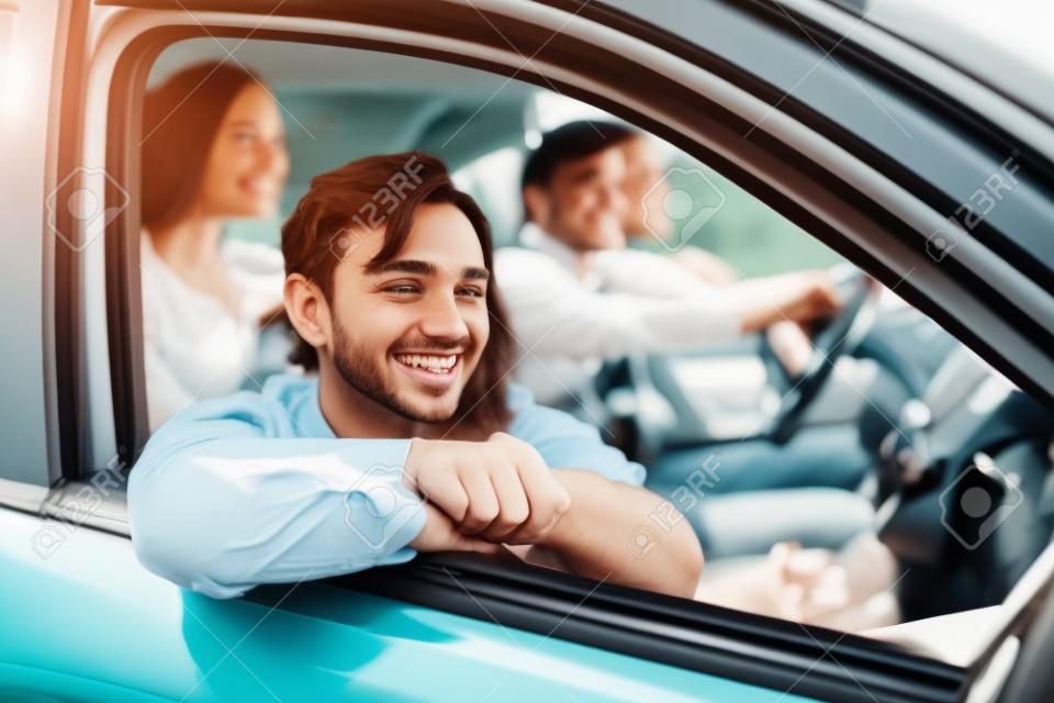 Bella giovane coppia seduta sui sedili del passeggero anteriore e sorridente mentre un bell'uomo alla guida di un'auto