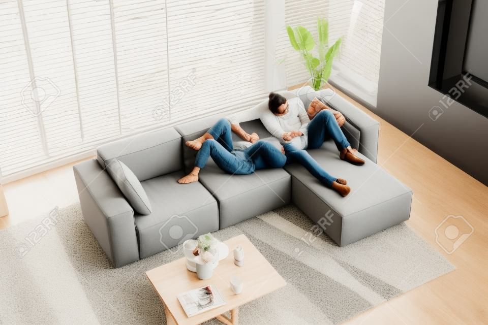Loving couple holding hands, relaxing on cozy sofa in modern living room top view, happy beautiful woman and man resting on comfortable couch together, spending lazy weekend, enjoying leisure time