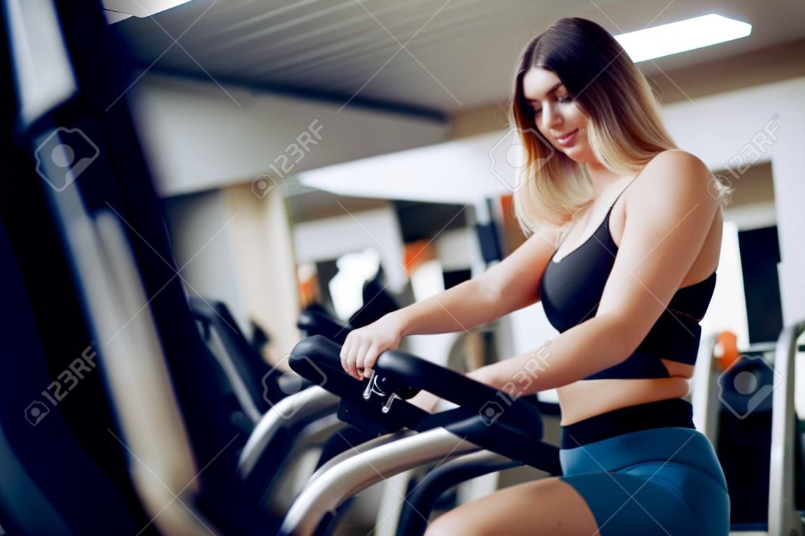 Fit curvy young blonde woman training in a cardio zone in a gym