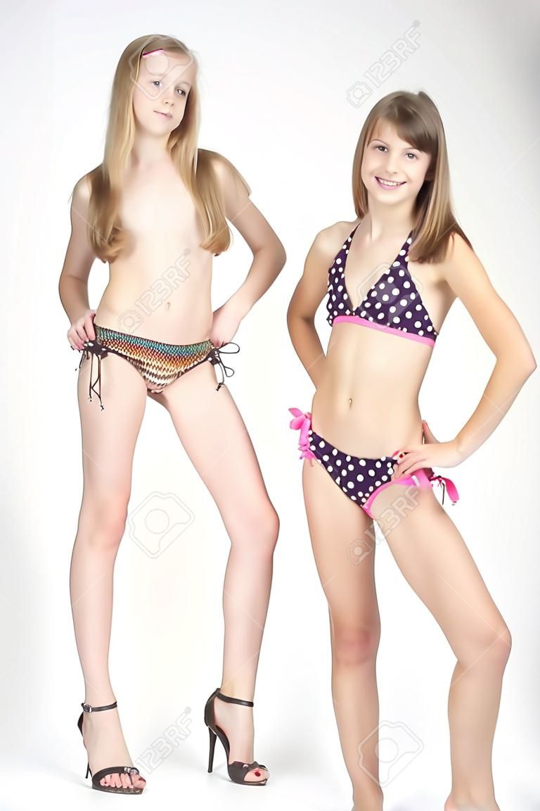 Две девочки подростки позирует в бикини и каблуки на белом фоне студии