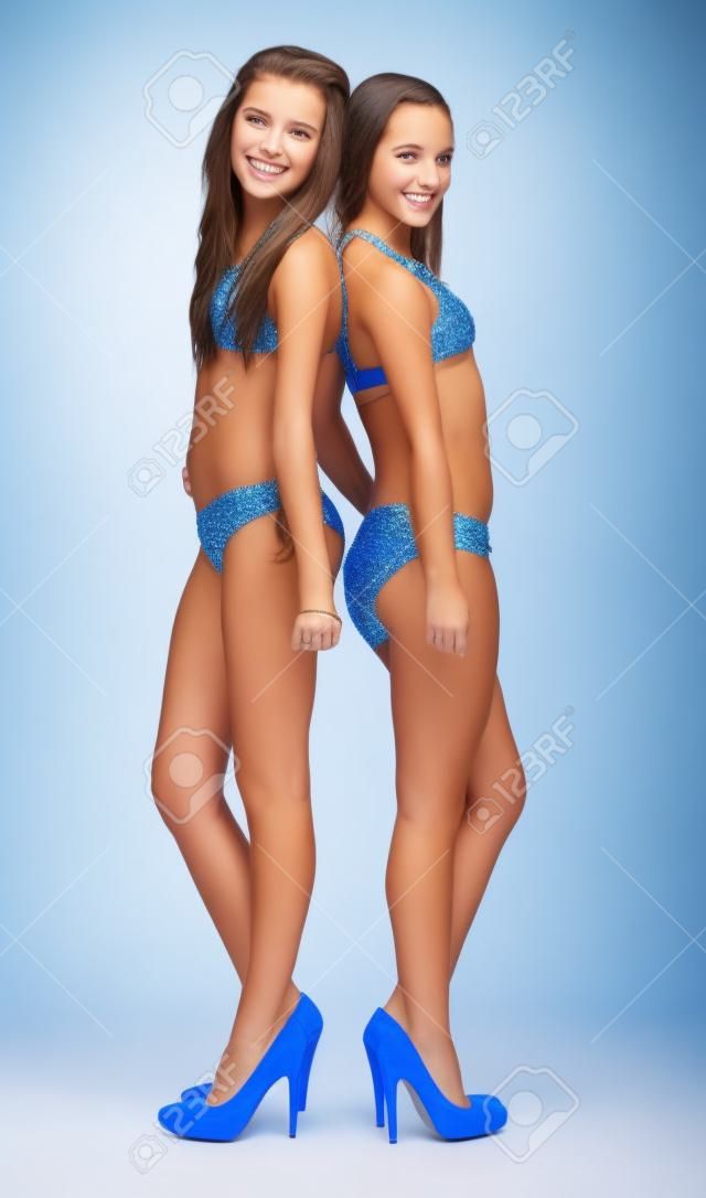 Deux adolescentes posant en bikini et talons contre un fond blanc studio