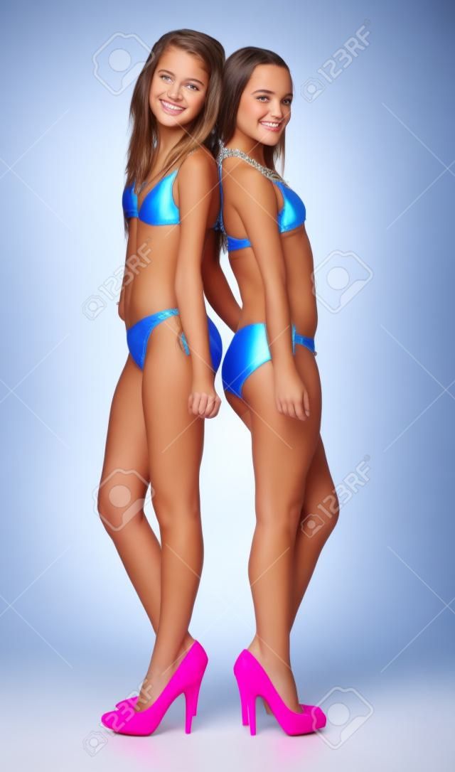 Deux adolescentes posant en bikini et talons contre un fond blanc studio