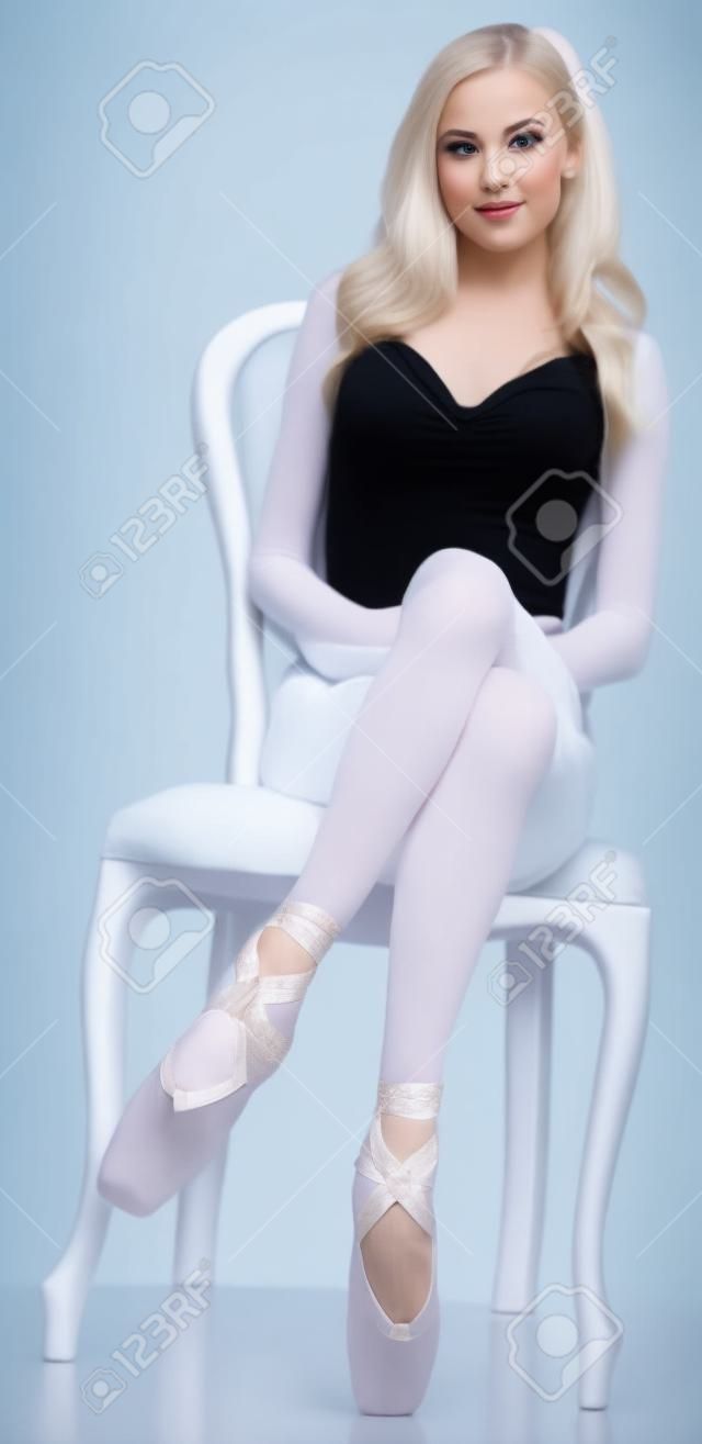Danseuse de ballerine posant sur une chaise contre un fond blanc studio