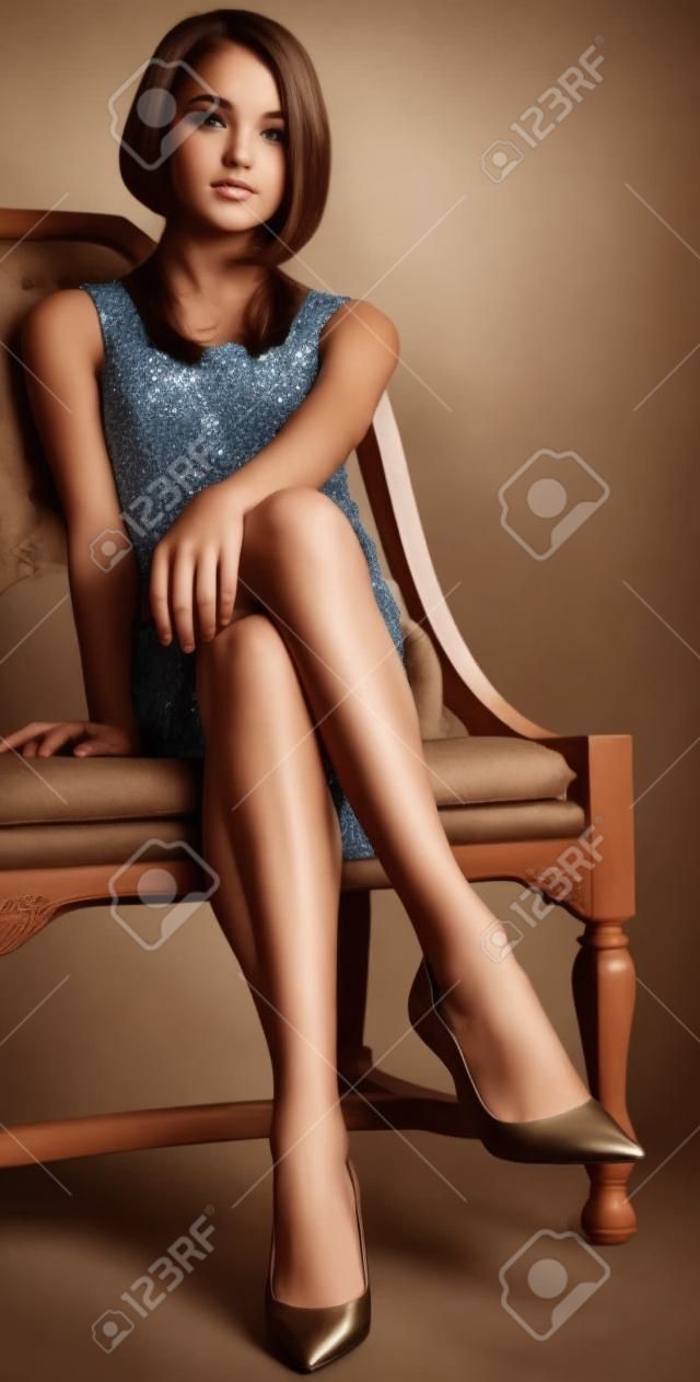 Chica bonita adolescente en una falda y tacones corto sentado con las piernas cruzadas