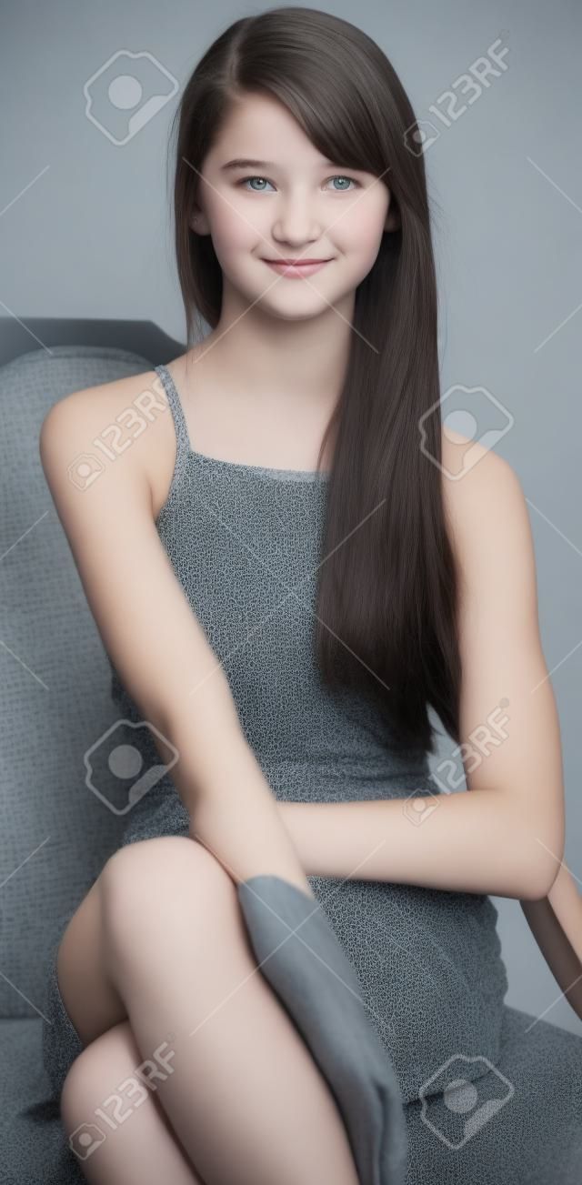 Muchacha adolescente que se sienta en un vestido gris