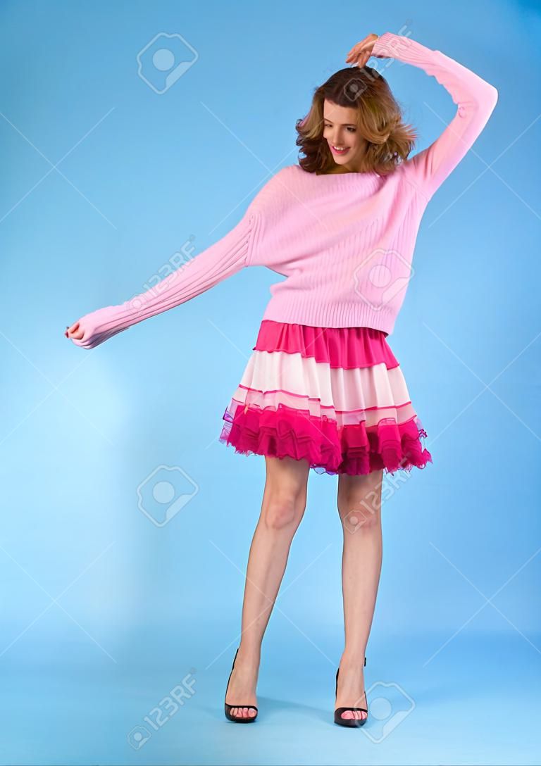 Modelo adolescente feliz y despreocupado posando falda rosa y suéter sobre un fondo azul