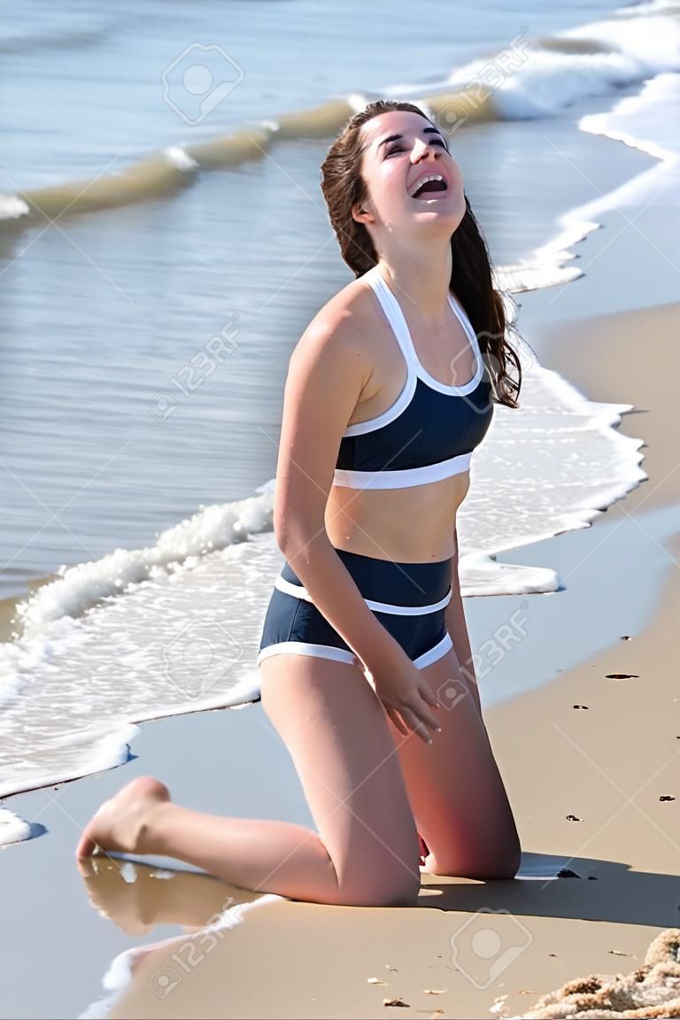 여자 bruenette 바다를 직면 하 고 웃 고 해변에 무릎을 꿇 고있다.