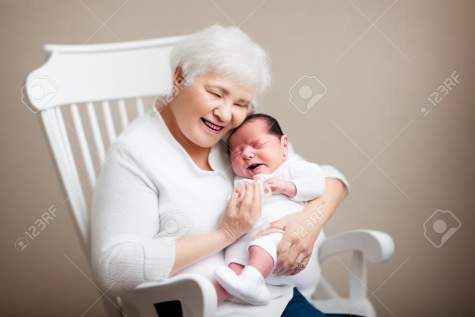 Hermosa abuela cantar a su nieto recién nacido sentado en una mecedora blanca