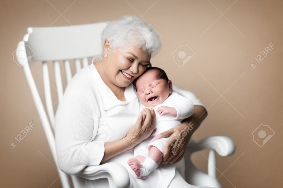 아름 다운 할머니는 흰색 흔들 의자에 앉아 그녀의 신생아 아기 손자 노래