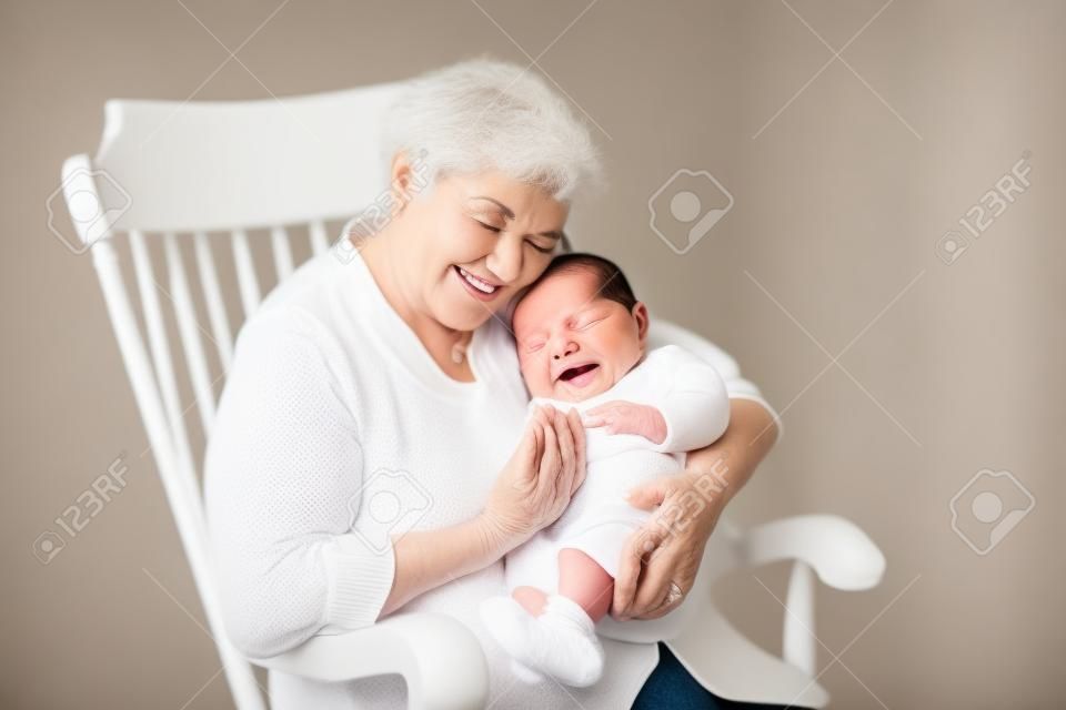 아름 다운 할머니는 흰색 흔들 의자에 앉아 그녀의 신생아 아기 손자 노래