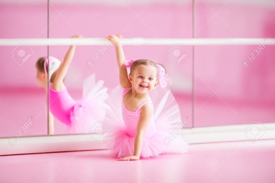 Kis balerina lány egy rózsaszín szoknyában. Imádnivaló gyermek tánc klasszikus balett, fehér stúdióban. Gyermekek táncolni. Gyerekek teljesítő. Fiatal tehetséges táncos egy osztályban. Óvoda gyerek vesz művészeti leckéket.