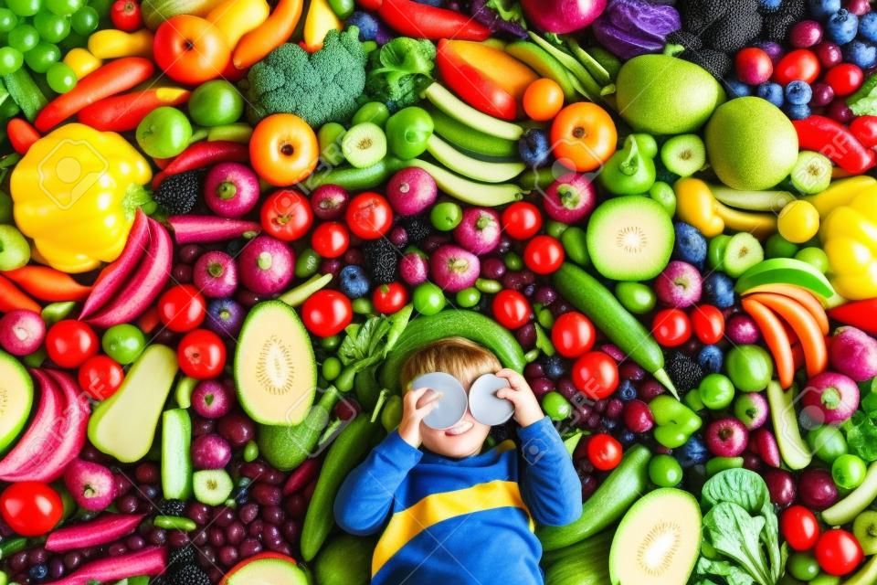 Little boy with variety of fruit and vegetable. Colorful rainbow of raw fresh fruits and vegetables. Child eating healthy snack. Vegetarian nutrition for kids. Vitamins for children. View from above.