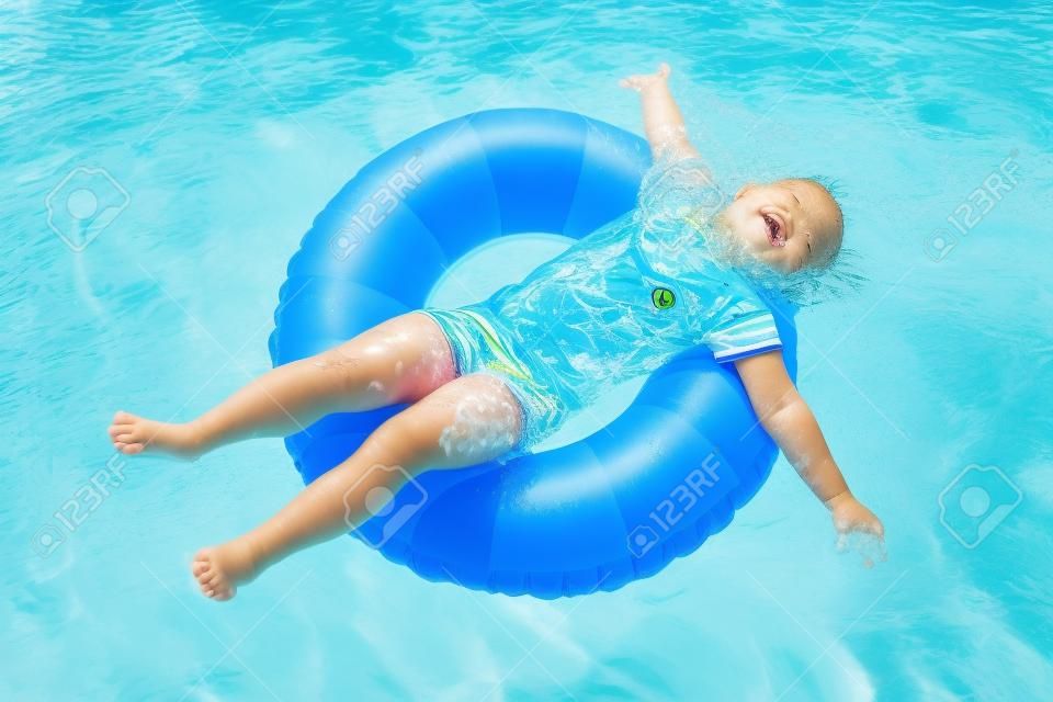 夏の暑い日に屋外スイミング プールでカラフルなインフレータブル リングと遊ぶ幸せな女の子。子供たちは泳げるようになります。子供の身に着けている太陽保護ラッシュ ガード リラックスできるトロピカル リゾートで