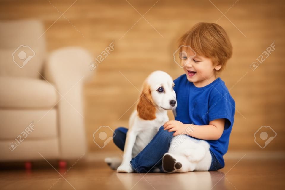 Criança brincando com cachorro bebê. Crianças brincam com filhote de cachorro. Menino e cocker americano spaniel no sofá em casa. Crianças e animais de estimação em casa. Criança sentada no chão com animal de estimação. Cuidados com os animais.