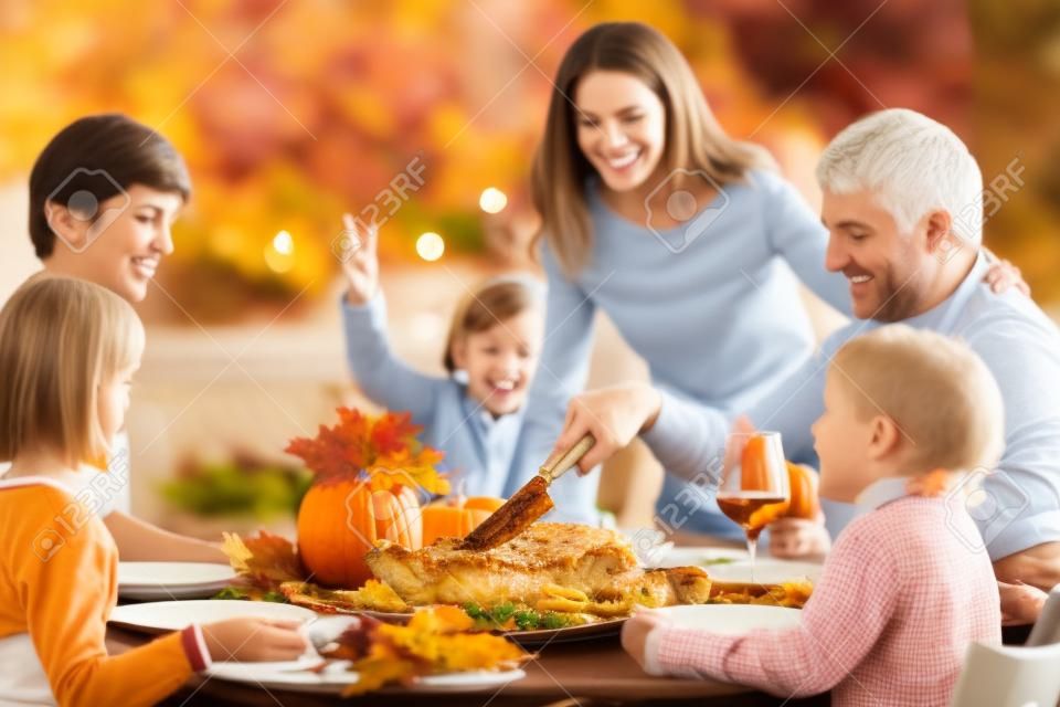 Familia con niños comiendo cena de Acción de Gracias. Pastel de calabaza y pavo asado en la mesa de comedor con decoración otoñal. Padres e hijos con comida festiva. Padre y madre cortando carne.