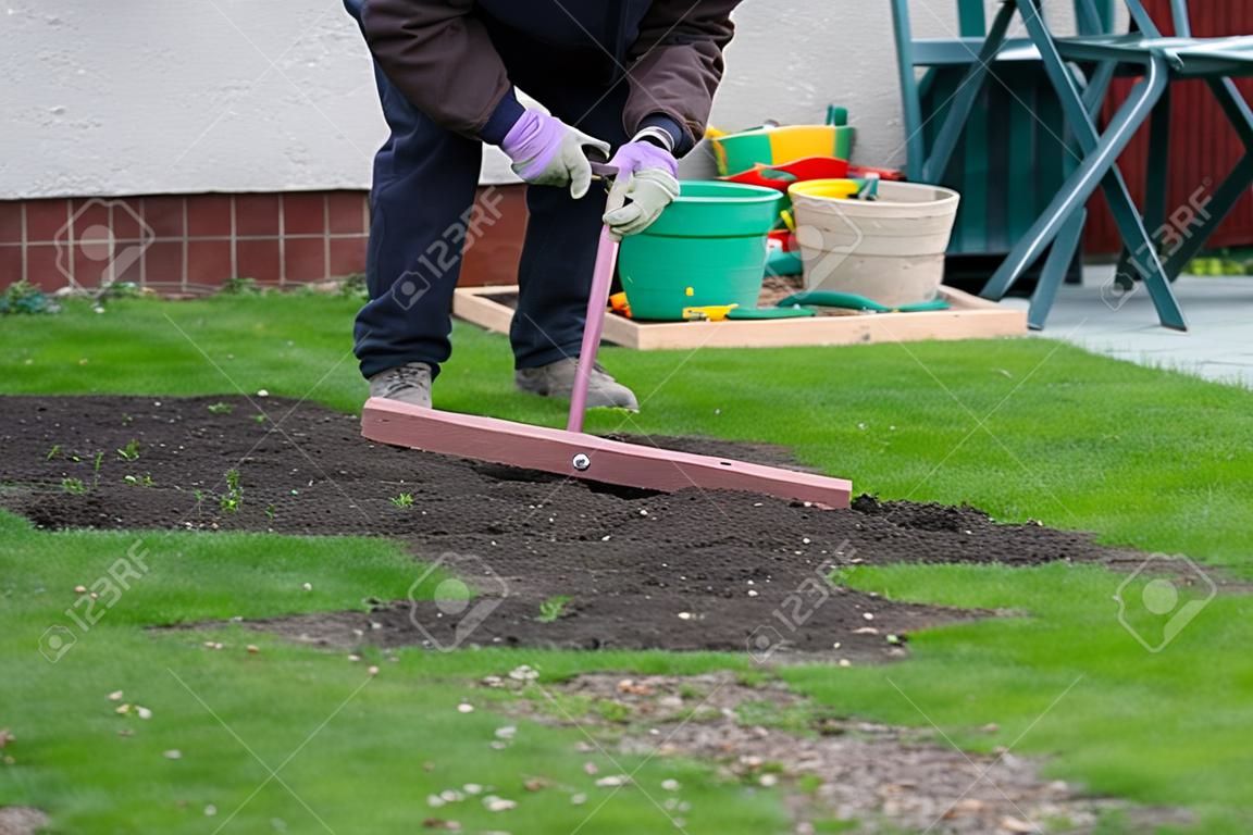 Important work after winter. Man add earth on garden and then aligning the surface with special tool. The tool is create from iron stick and wooden board. Summer landscaping in the garden.