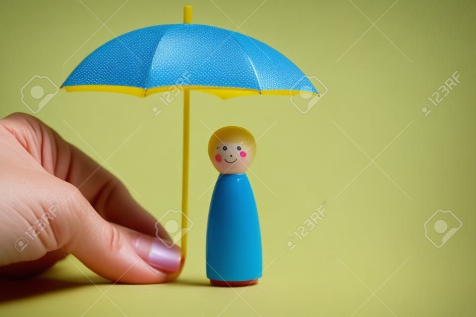 Mano che tiene ombrello giallo con bambola piolo ragazza su sfondo blu. il concetto di copertura assicurativa. il concetto di autoprotezione