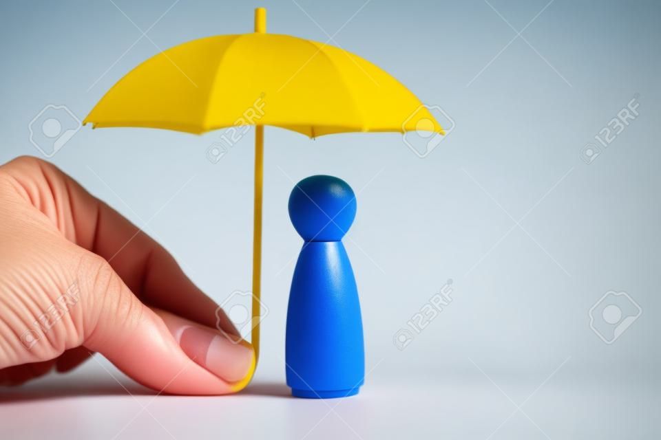Mano che tiene ombrello giallo con bambola piolo ragazza su sfondo blu. il concetto di copertura assicurativa. il concetto di autoprotezione