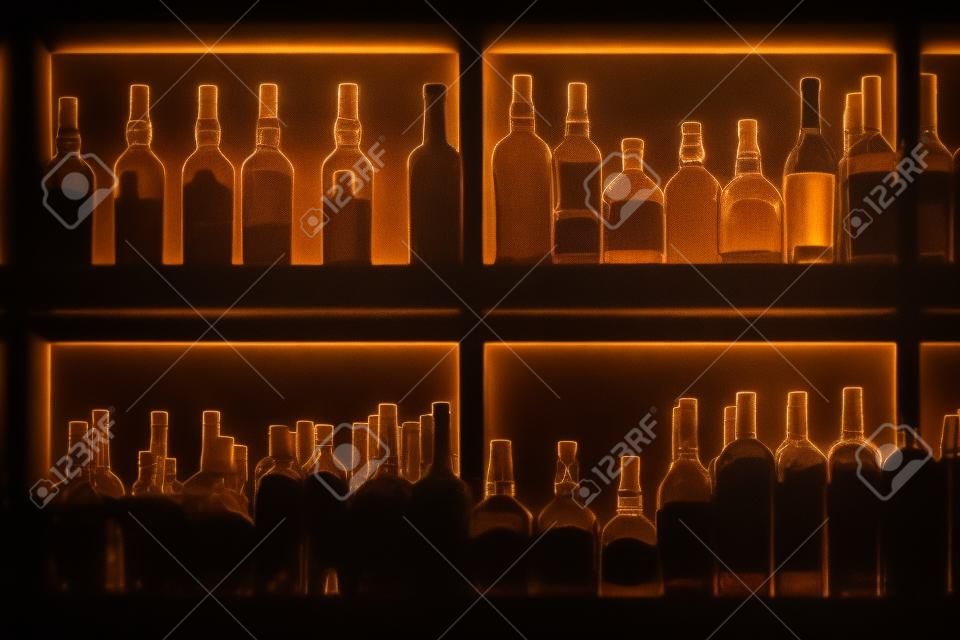 Butelki stojące na półce w barze, podświetlane od tyłu