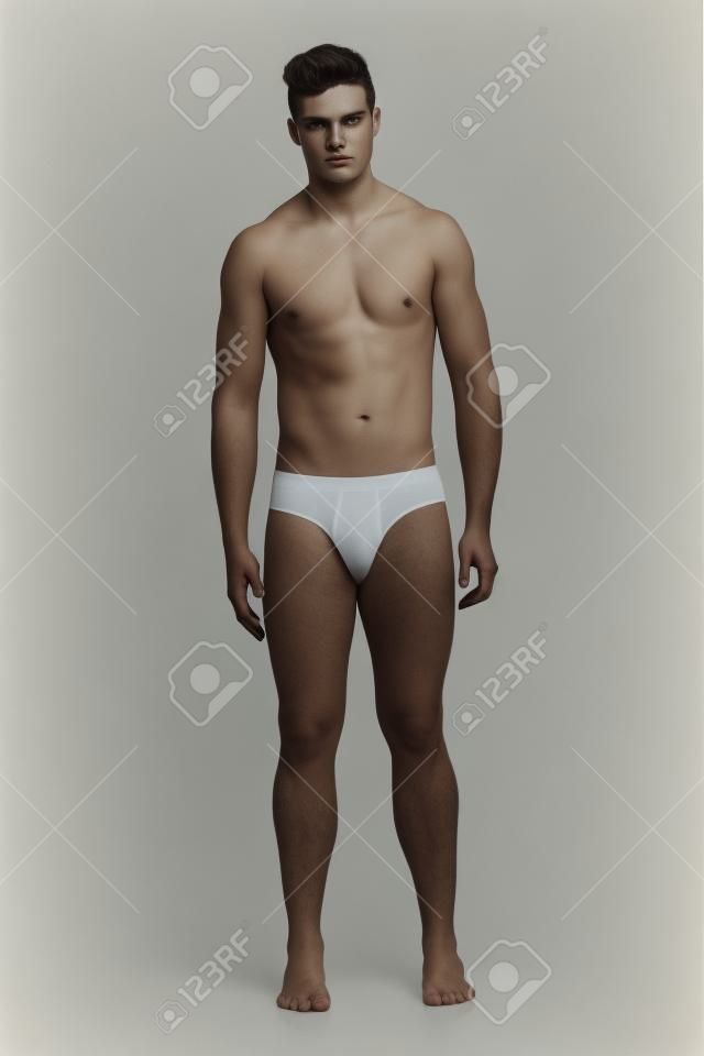in voller Länge Porträt von einem jungen Mann, der nichts als seine Unterwäsche und schaut in die Kamera, isoliert auf weiß
