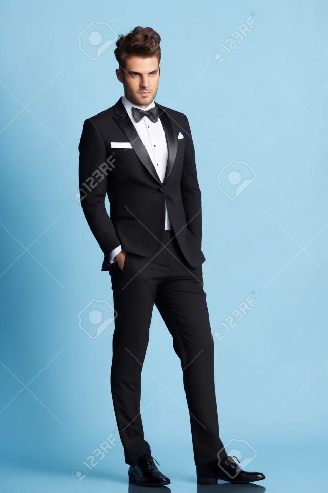 relaxed elegant man in tuxedo looking at the camera on white background