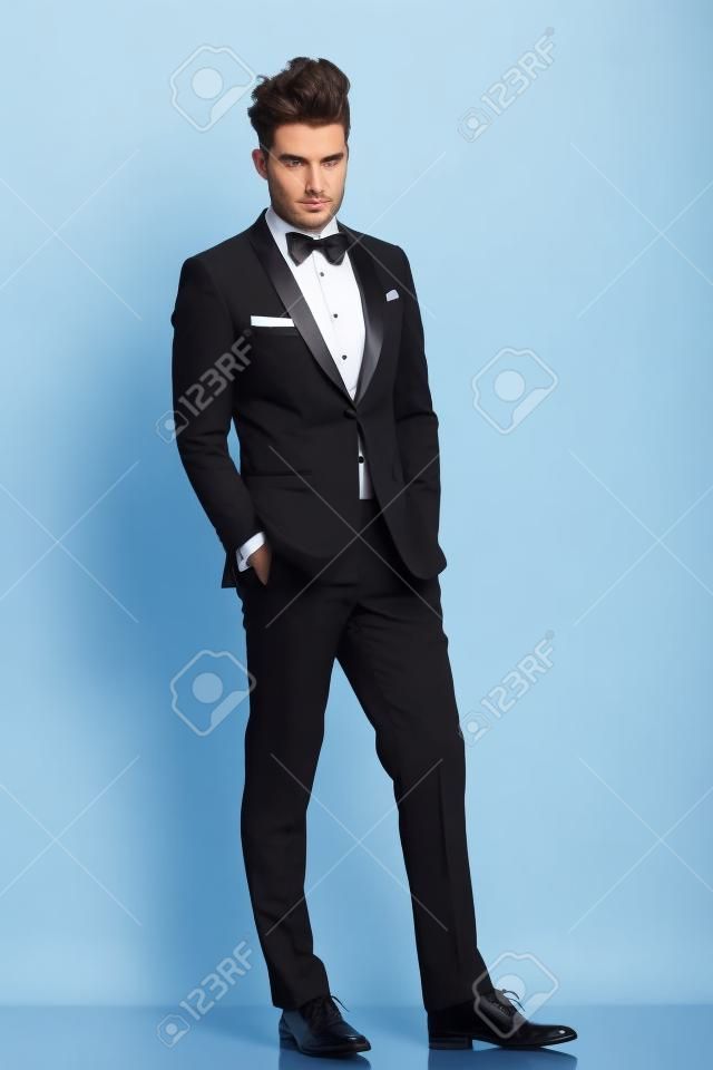 relaxed elegant man in tuxedo looking at the camera on white background