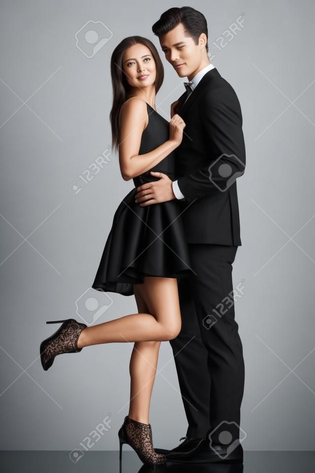 side view of embraced elegant couple in black clothes, woman looking back while holding her lover